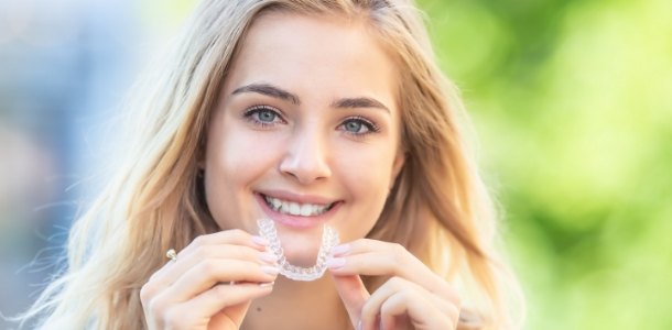 Smiling blonde woman holding clear aligners in Heber City