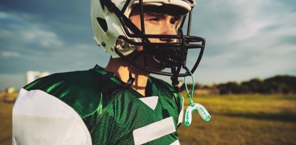 Football player with athletic mouthguard hanging from their helmet