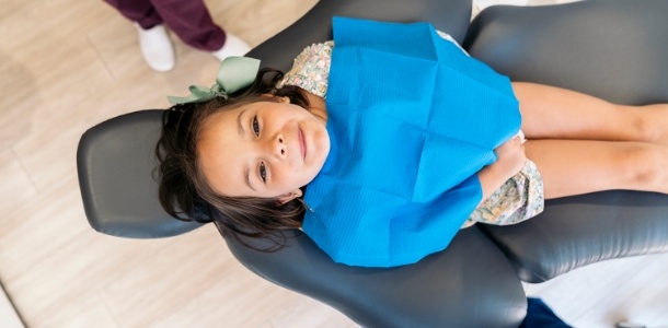 Young girl in dental chair smiling up at the camera