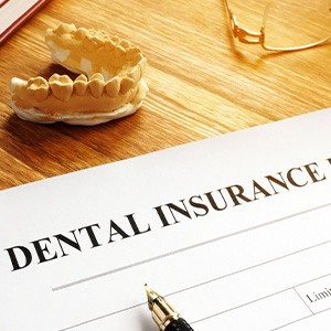 Dental insurance form on desk with model of teeth and glasses