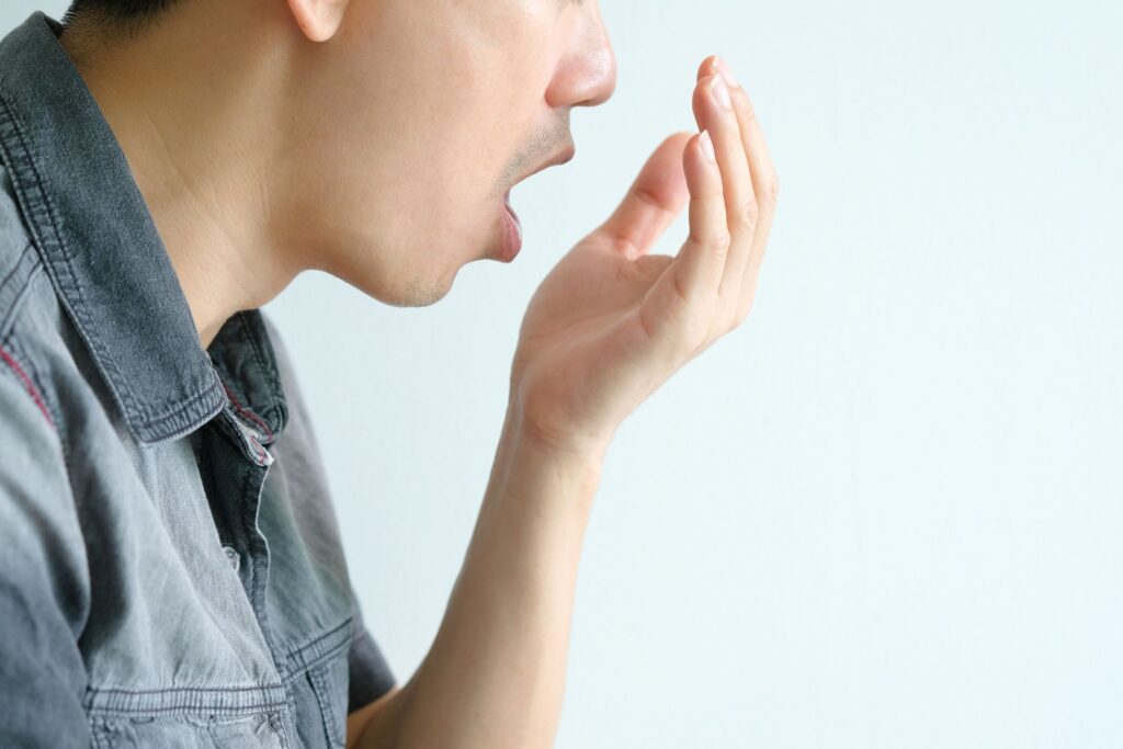 Profile view of man in gray shirt trying to smell his own breath